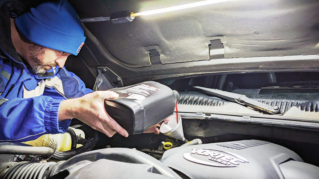 male adding fluids to a vehicles engine at night lit up by the STKR Underhood light.