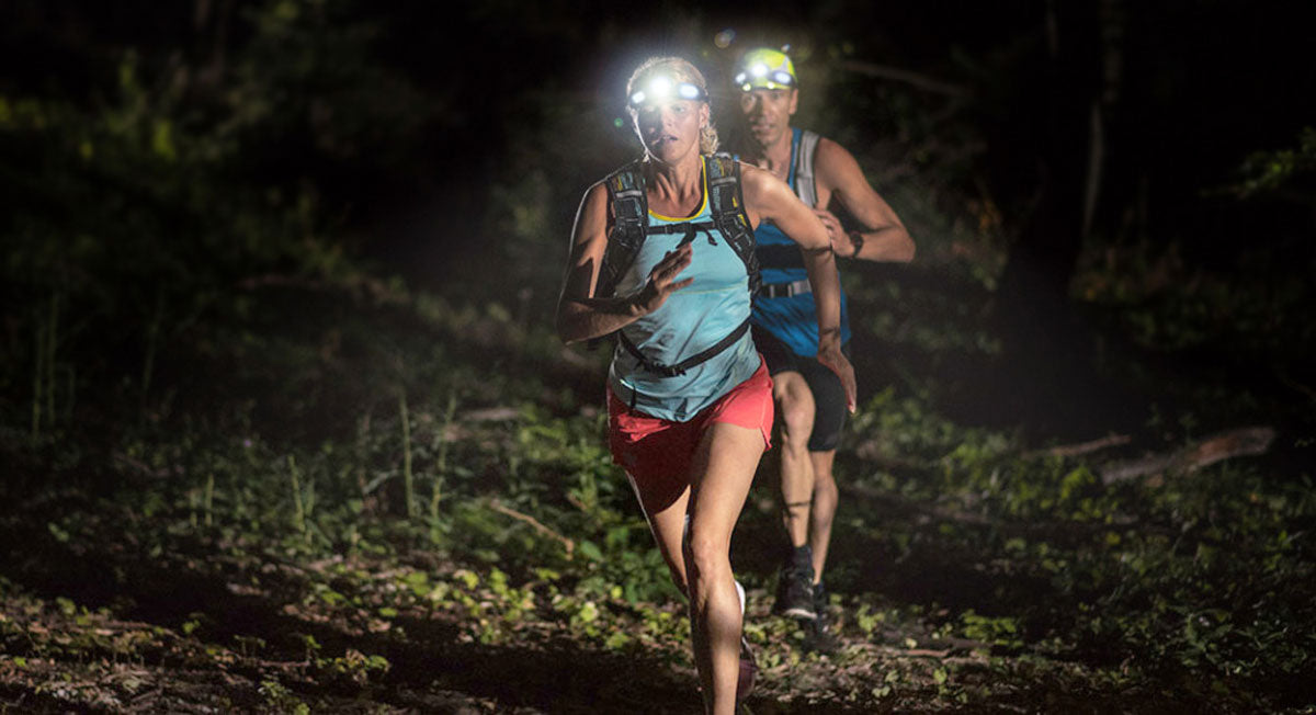 lifestyle image of a female and male running a forest trail at night both wearing FLEXIT Headlamps