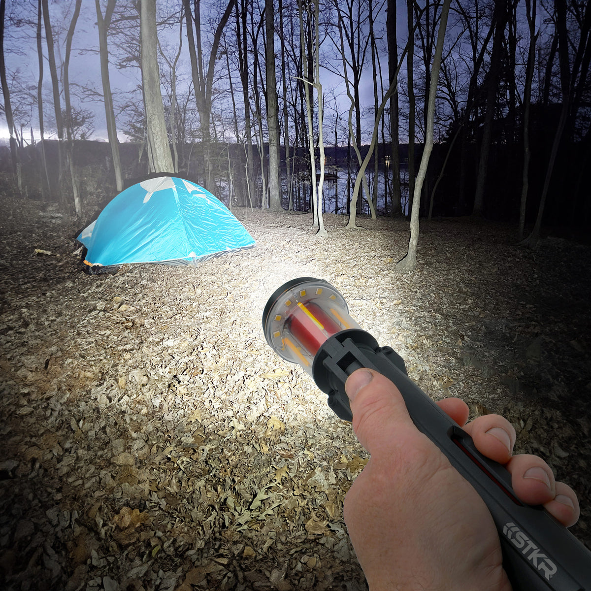 Person holding a FLi-MORPHE flashlight in a forest with a blue tent in the background