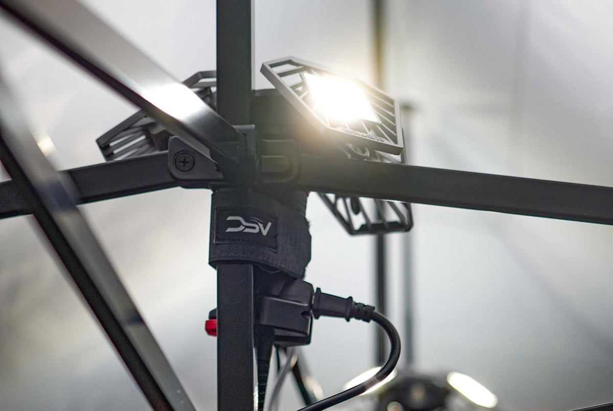 ShopLight V2 mounted to a pop-up canopy frame and lighting a booth, power cord visible.