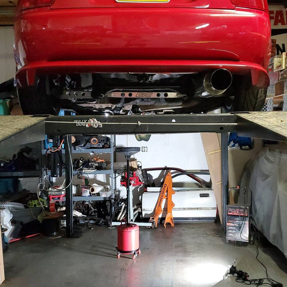 Red car on a lift in a garage with tools and equipment around. Shoplight V2 on the ground lighting up the bay.