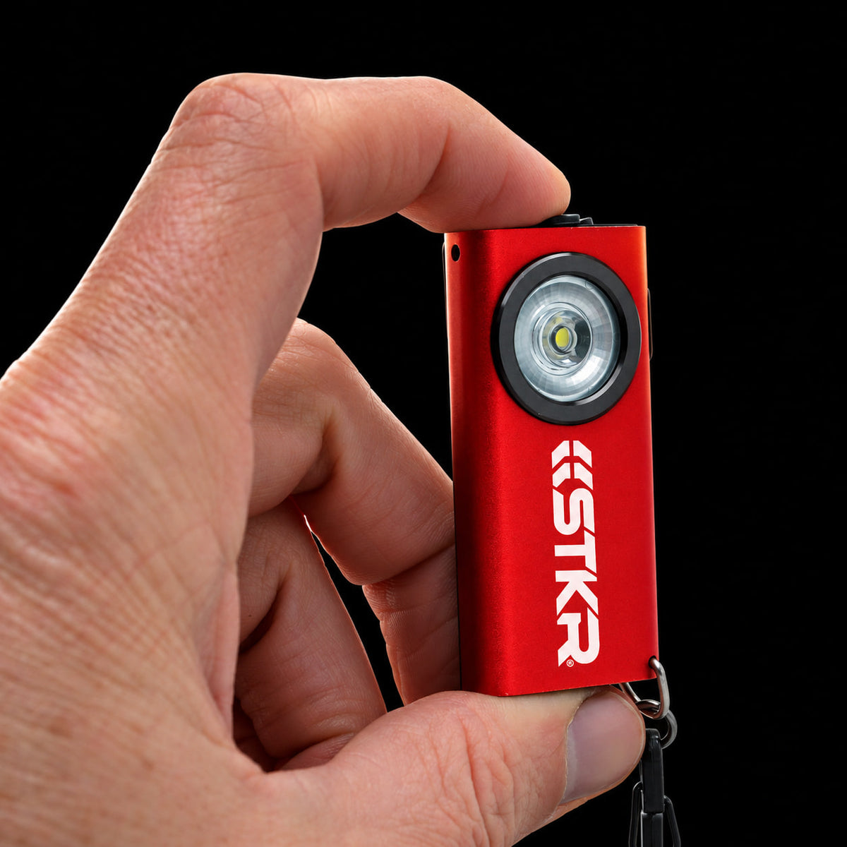 Red STKR SlimJIMMY keychain light held between two fingers to show its size