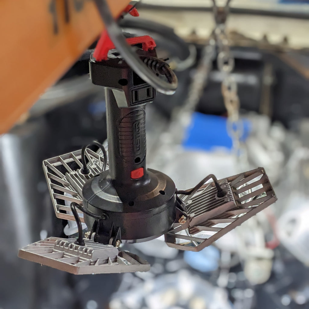 Under-hood engine work at night with ShopLight V2 hanging from an engine hoist, lighting the engine swap.