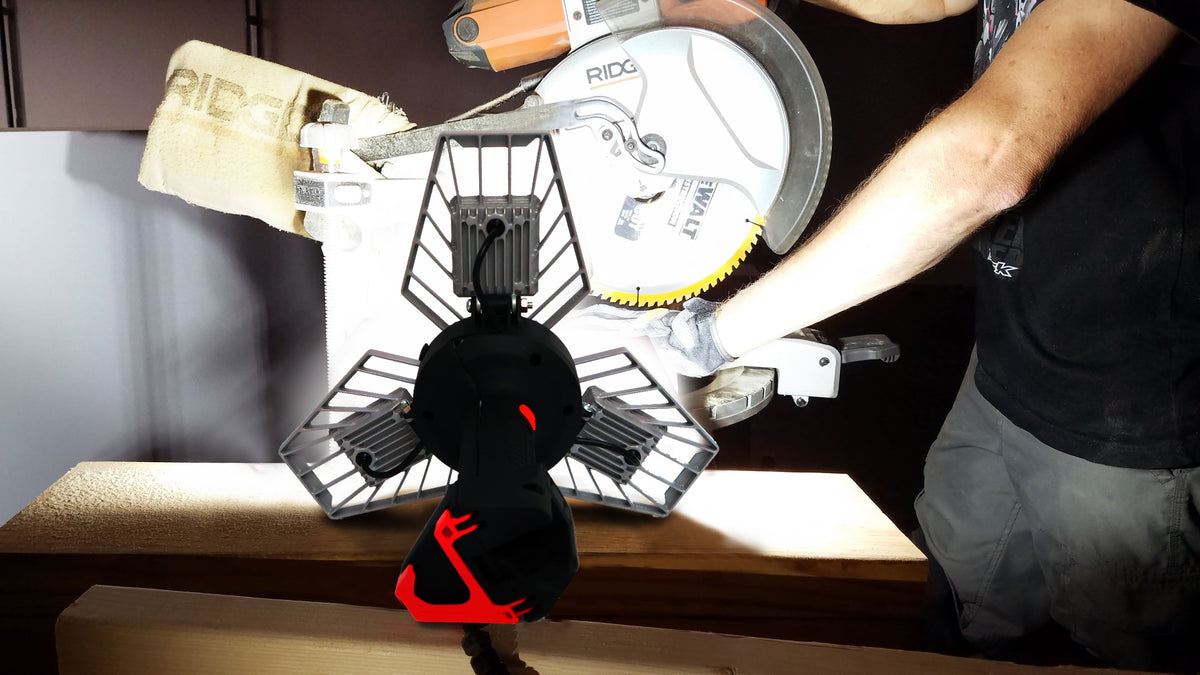 ShopLight V2 sitting near a miter saw with three heads lighting the cut line and workbench. Person using the saw.